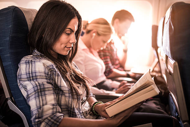 Young woman sitting in an airplane with other passengers and enjoying in a book.